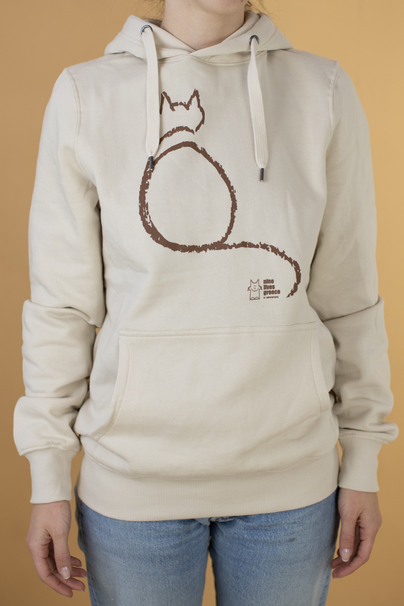 A model wearing a cream hoodie with brown print of a sitting cat.